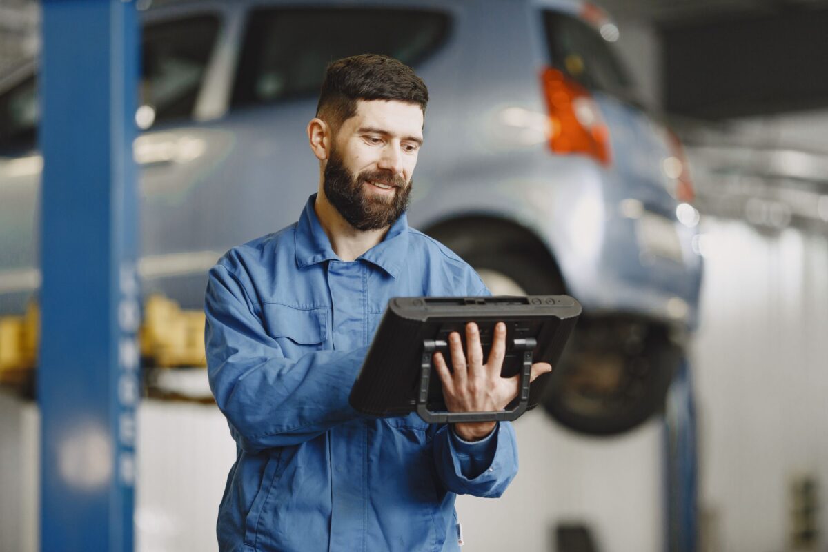 Smiling auto mechanic uses digital tablet in car repair shop environment.