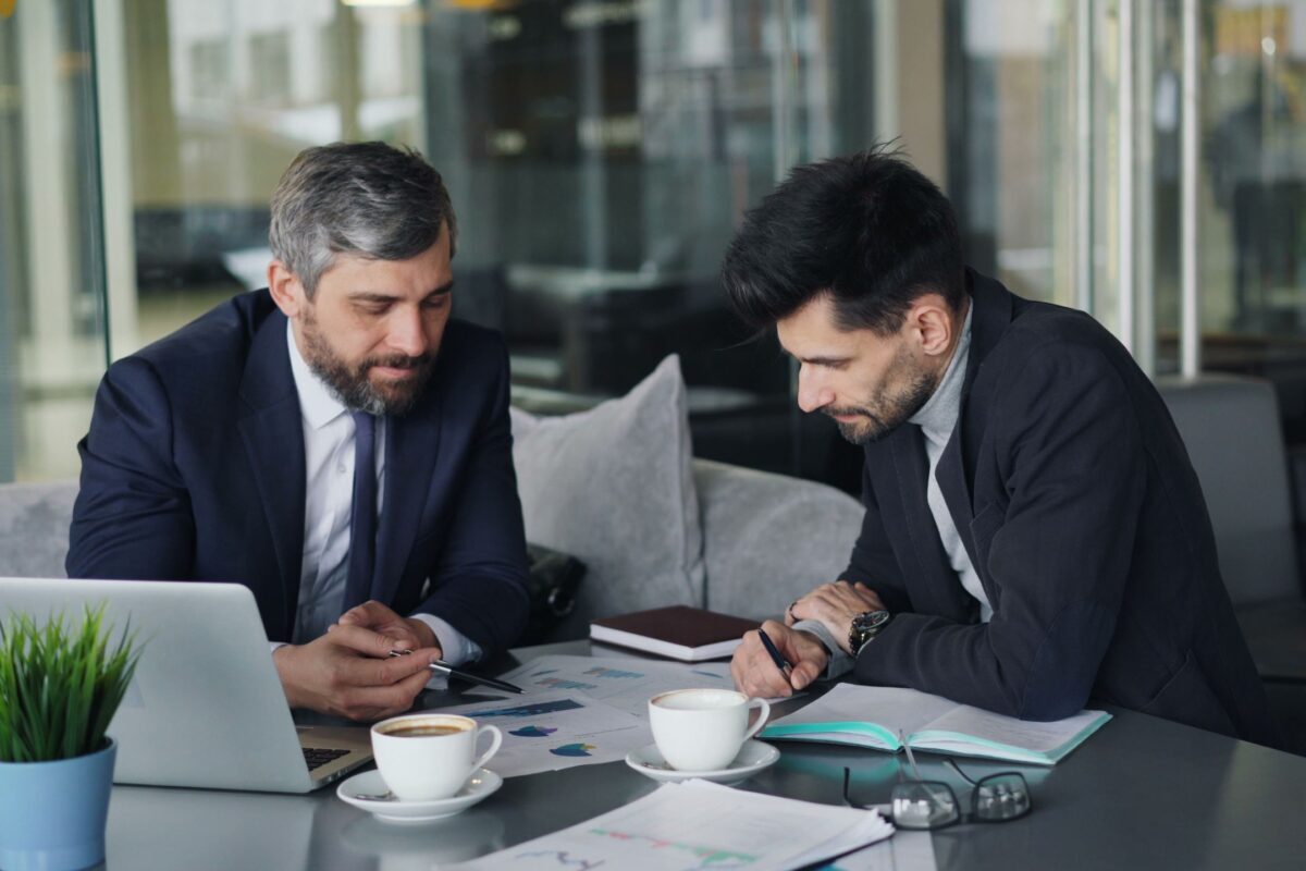 Two businessmen discussing charts over coffee at a café.